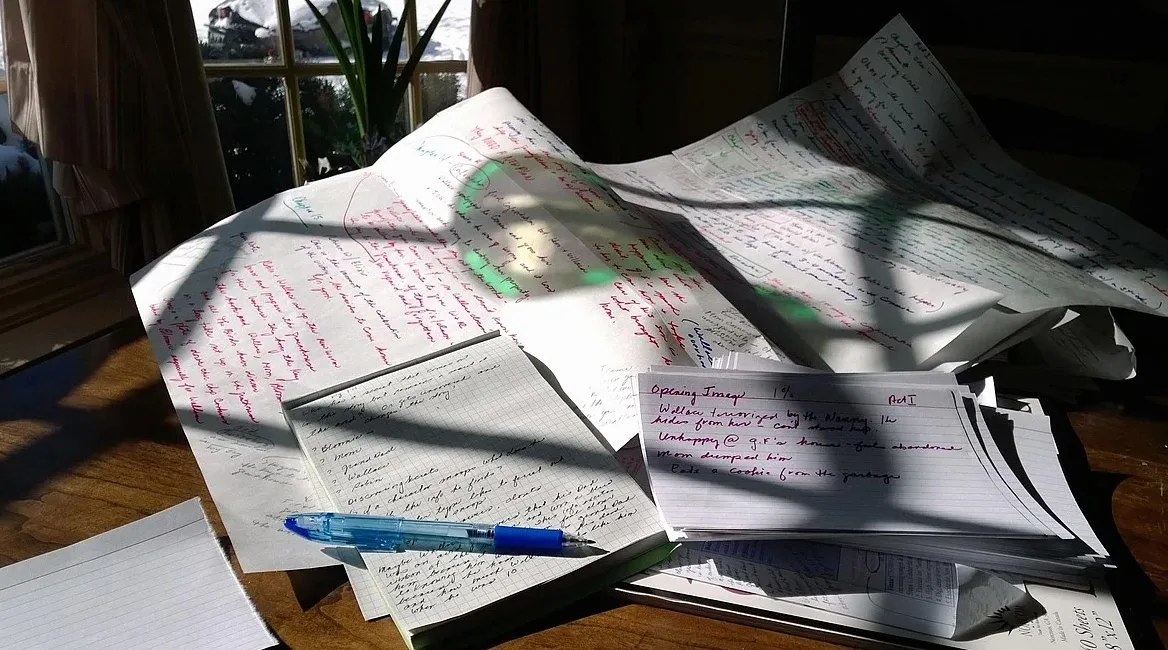 手書きのメモや紙が重なった机の上のペン